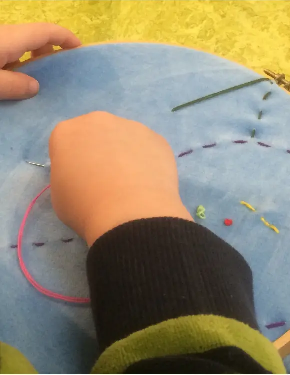 Barnhand som broderar färgglada stygn – skaparglädje i tidig ålder